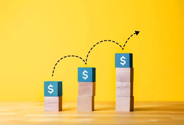 Is There an Amazon Honeymoon Period, and How Do I Grow Sales Fast? 1 A stack of wooden blocks on a yellow background with an arrow pointing to a dollar sign. The blocks represent the marketplace, showcasing effective marketing management by My Amazon Guy.