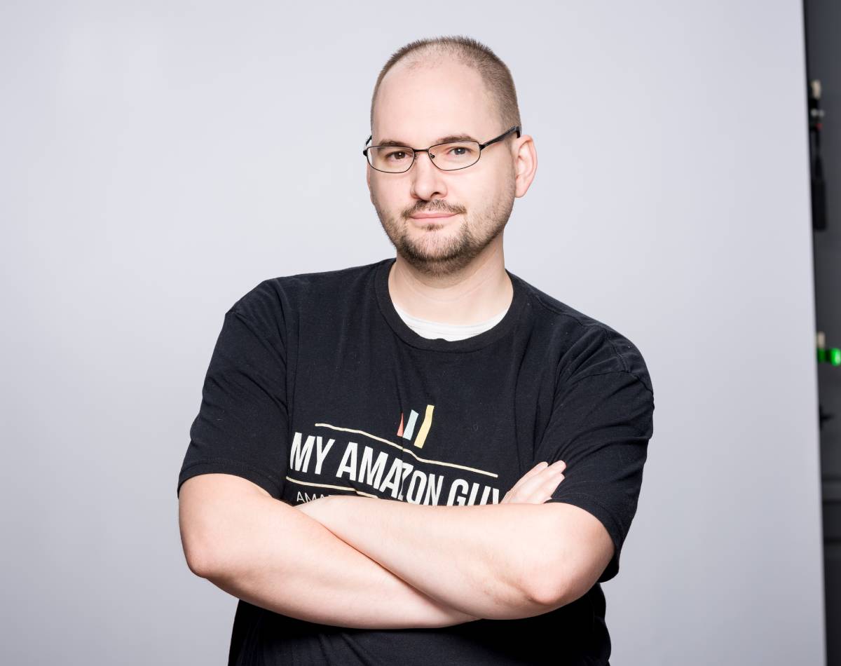 A man, wearing glasses and a black t-shirt, excels in marketing management and marketplace strategies.